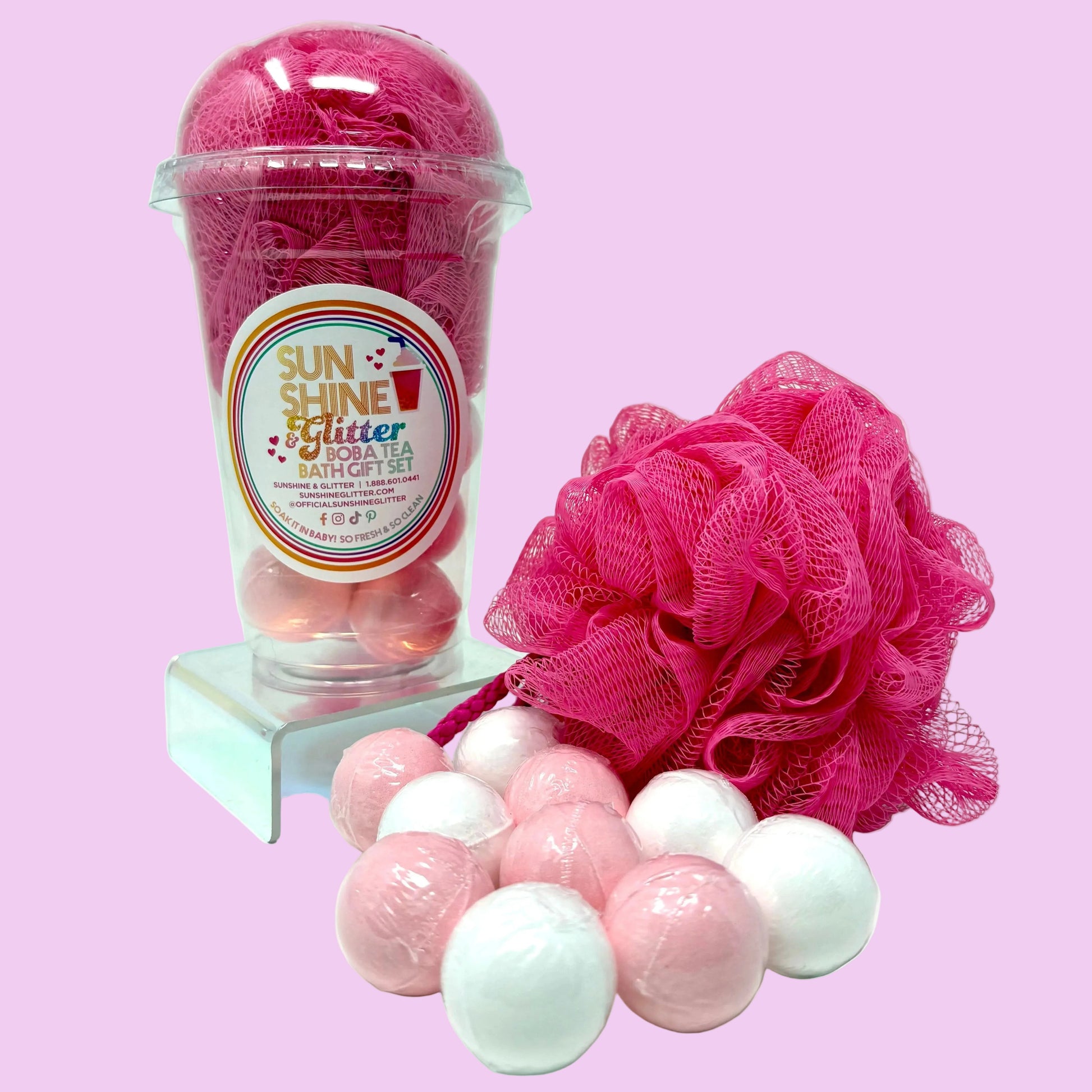 Bath gift set with pink bath bombs, loofah, and packaging on a white background